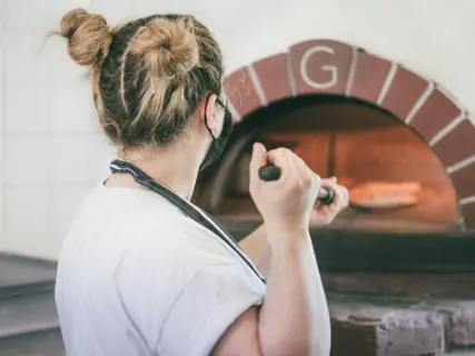 A pizzaiolo turning a pizza on the peel