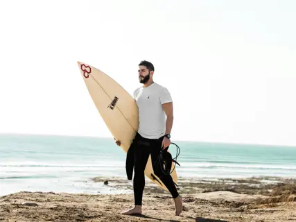A surfer in a wetsuit wading out with a board under one arm