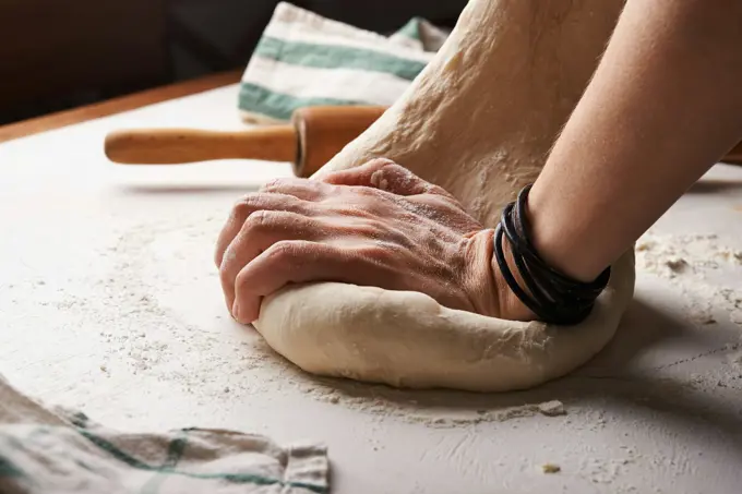 Hands working a ball of dough on a floured bench
